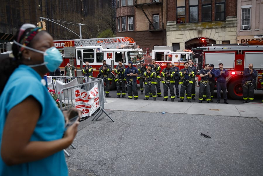FILE - In this April 14, 2020, file photo FDNY firefighters gather to applaud medical workers as attending physician Mollie Williams, left, wears personal protective equipment due to COVID-19 concerns outside Brooklyn Hospital Center in New York. Essential workers are lauded for their service and hailed as everyday heroes. But in most states nurses, first responders and frontline workers who get COVID-19 on the job have no guarantee they&#039;ll qualify for workers&#039; comp to cover lost wages and medical care.