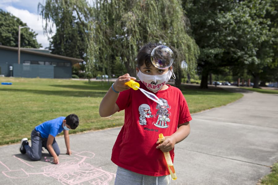 Alex Clemente, 10, of Ridgefield, background left, enjoys some time outside while putting the finishing touches on his chalk drawing while joined by his sister, Eva, 8, as she plays with bubbles during a day camp at the Marshall Community Center on Wednesday.