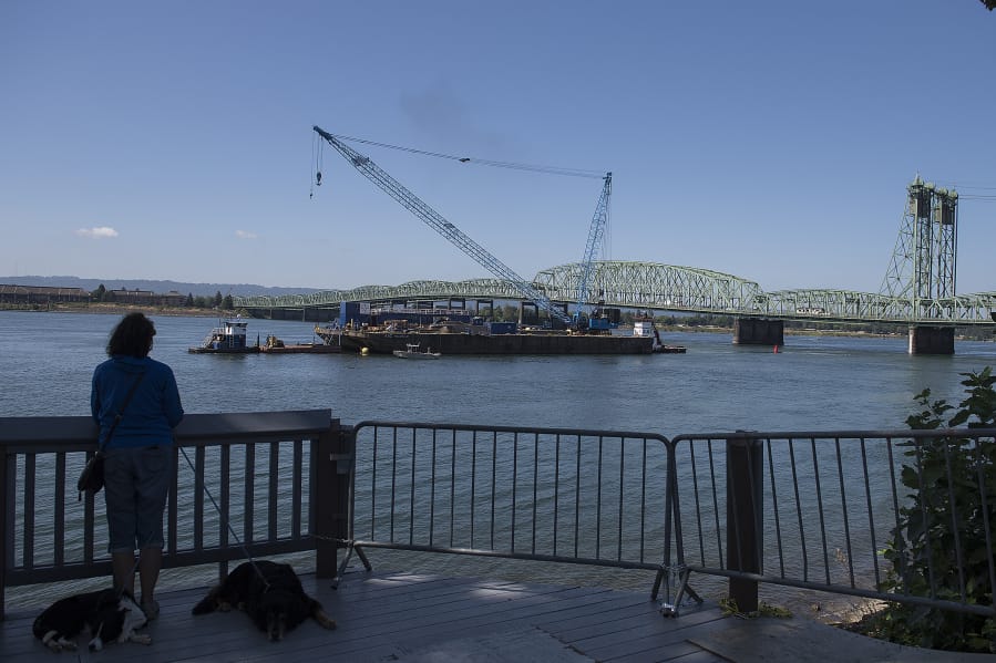 A person watches from the bank of the Columbia River as the trunnion, sheaves and other replacement components for the Interstate 5  Bridge arrive in Vancouver via barge on Tuesday morning.