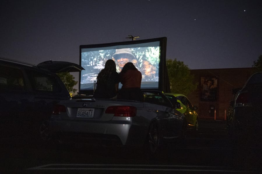 Alexa Malone, left, and Maryam Ali, right, both 17 and of Camas, sit atop their friendis convertible as they watch &quot;Raiders of the Lost Ark&quot; during the Pop Up Cinema in the Vancouver Mall parking lot on Friday.