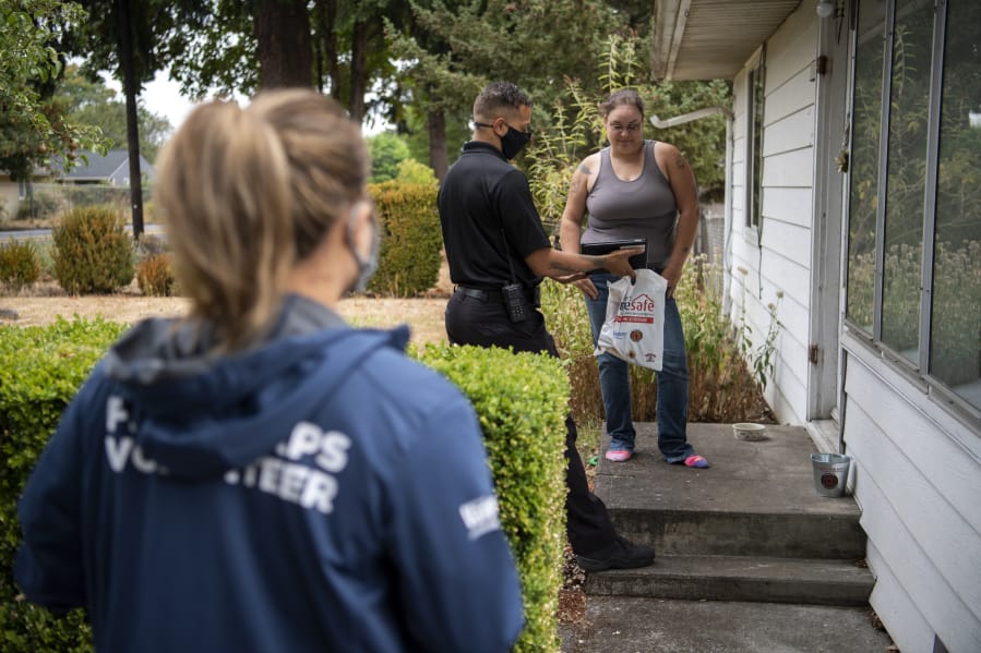 Vancouver Deputy Fire Marshal LeMont Lucas, center, shows a brief fire-safety video to Katie Jefferson outside her home Saturday morning. Firefighters and volunteers with the Vancouver Fire Department canvas Vancouver neighborhoods every week to disseminate fire safety information and hand out souvenir reminders.