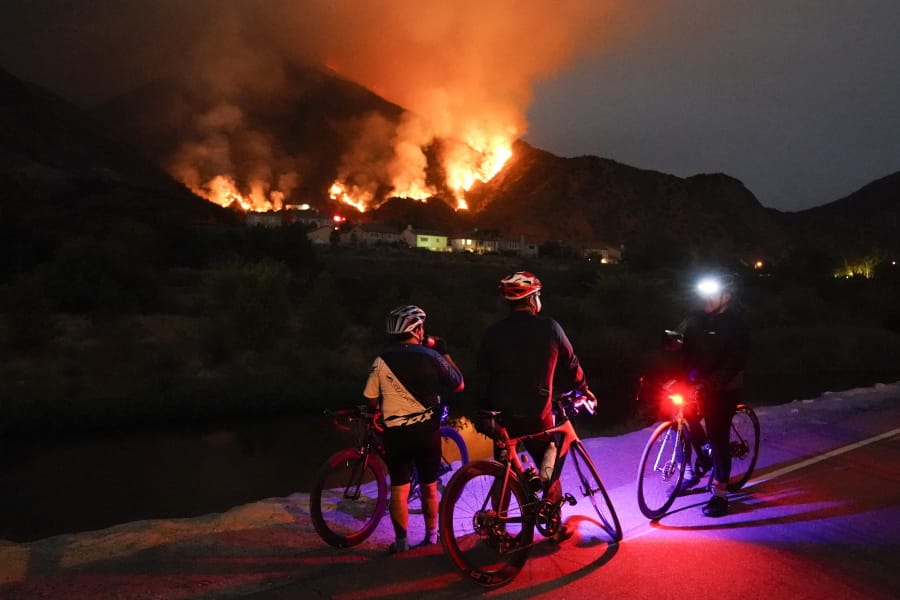 Cyclists rest along a trail as the Ranch Fire burns, Thursday, Aug. 13, 2020, in Azusa, Calif. Heat wave conditions were making difficult work for fire crews battling brush fires and wildfires across Southern California.