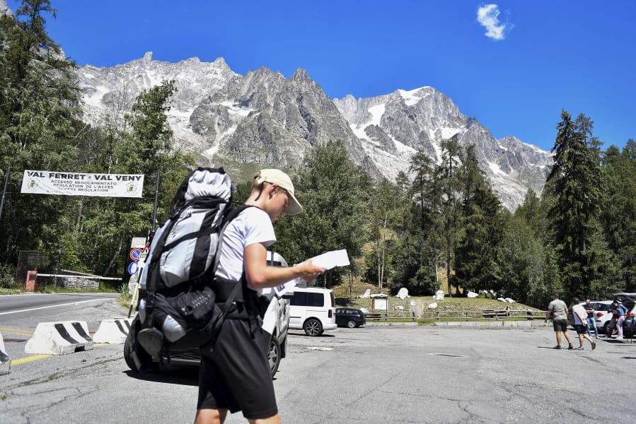 A hiker looks at a map as he walks in a parking lot beneath the Planpincieux glacier, seen at background right, in the Alps on the Grande Jorasses peak of the Mont Blanc massif, in Val Ferret on the south side of the Mont Blanc, near Courmayeur, northern Italy, Friday, Aug. 7, 2020. Some 70 people were evacuated Thursday in the valley below the glacier and roads closed after the threat of collapse the the fast-moving melting glacier is posing to the picturesque valley near the Alpine town of Courmayeur.