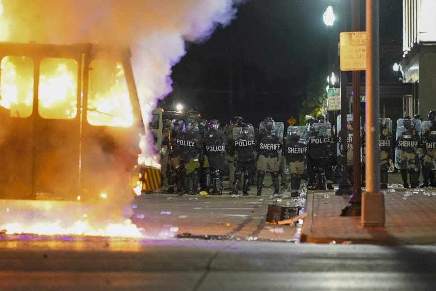 Police stand near a garbage truck ablaze during protests, Monday, Aug. 24, 2020, in Kenosha, Wis., sparked by the shooting of Jacob Blake by a Kenosha Police officer a day earlier.