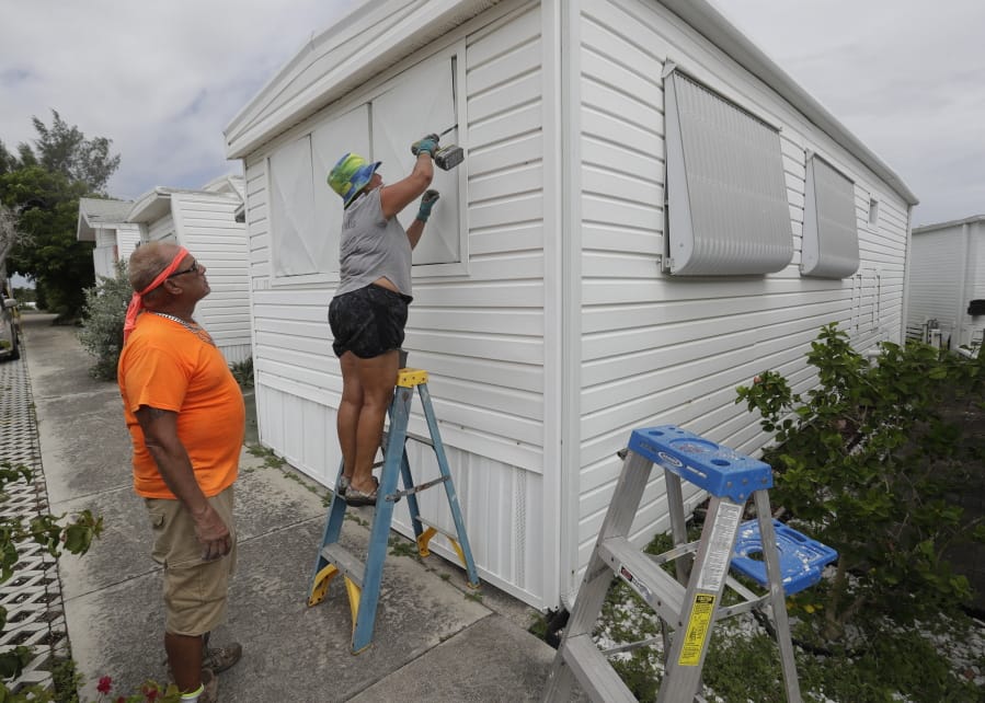 Chris Nagiewicz, left, watches as his wife Mary screws in a hurricane panel, Saturday, Aug. 1, 2020, on a trailer home in Briny Breezes, Fla. Hurricane Isaias is headed toward the Florida coast, where officials have closed beaches, parks and coronavirus testing sites. The husband and wife handyman team maintain about 50 trailers including their own and plan to spend the hurricane in a hotel.