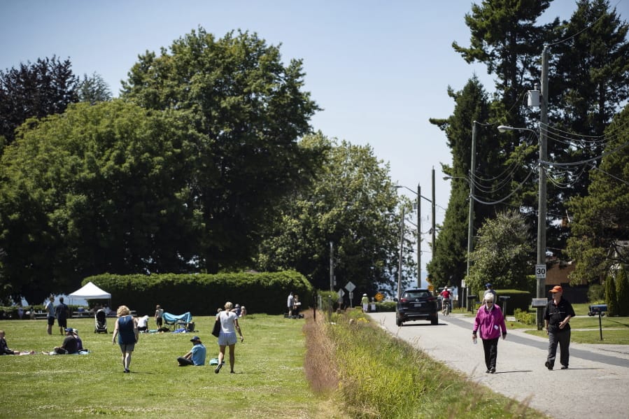 A ditch marks the Canada-U.S. border and separates people walking on the road, right, in Surrey, British Columbia, and those gathered at Peace Arch Historical State Park, left, in Blaine, Wash., Sunday, July 5, 2020. Although the B.C. government closed the Canadian side of the park in June due to concerns about crowding and COVID-19, people are still able to meet in the U.S. park due to a treaty signed in 1814 that allows citizens of Canada and the U.S. to unite in the park without technically crossing any border.