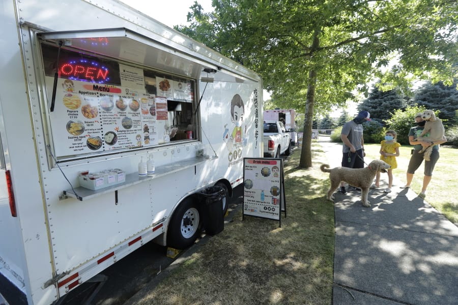 Bobby Price, left, and Catherine Vogt, right, stand with Catherine&#039;s daughter Avery, 8, and their dogs as they wait to order from the YS Street Food food truck, Monday, Aug. 10, 2020, near the suburb of Lynnwood, Wash., north of Seattle. Long seen as a feature of city living, food trucks are now finding customers in the suburbs during the coronavirus pandemic as people are working and spending most of their time at home. (AP Photo/Ted S. Warren) (Ted S.