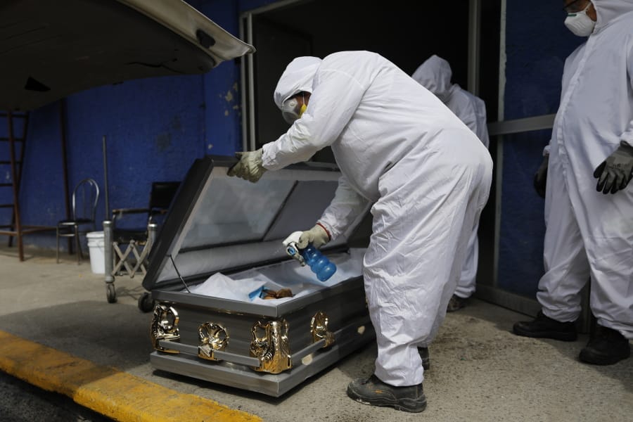A worker wearing protective gear sprays disinfectant solution inside the coffin of a person who died from suspected COVID-19, as the body arrives Monday at the crematorium at Xilotepec Cemetery in Xochimilco, Mexico City.