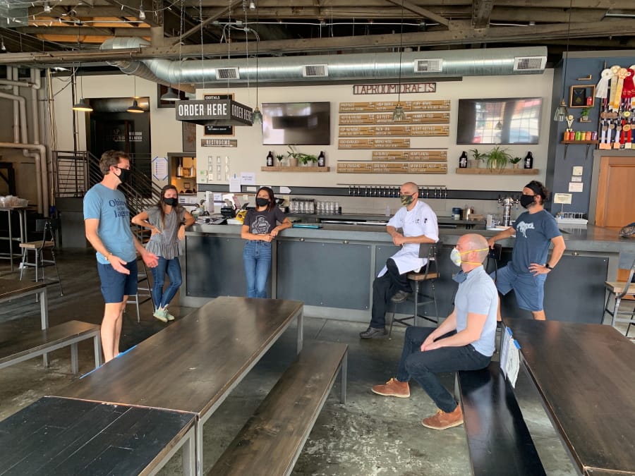 In a July 2020 photo provided by Wolf&#039;s Ridge Brewing, owner Bob Szuter, employees Allison Randolph and Alicia Herrmann, sous chef Andy Zamagias, general manager Corey Schlosser and employee Andy Powell, from left, gather inside the restaurant&#039;s tap room in Columbus, Ohio. Szuter says he&#039;s trying to figure out new ways to bring in revenue, focusing more on the brewery side of the business until it&#039;s safe to have a full dining room.