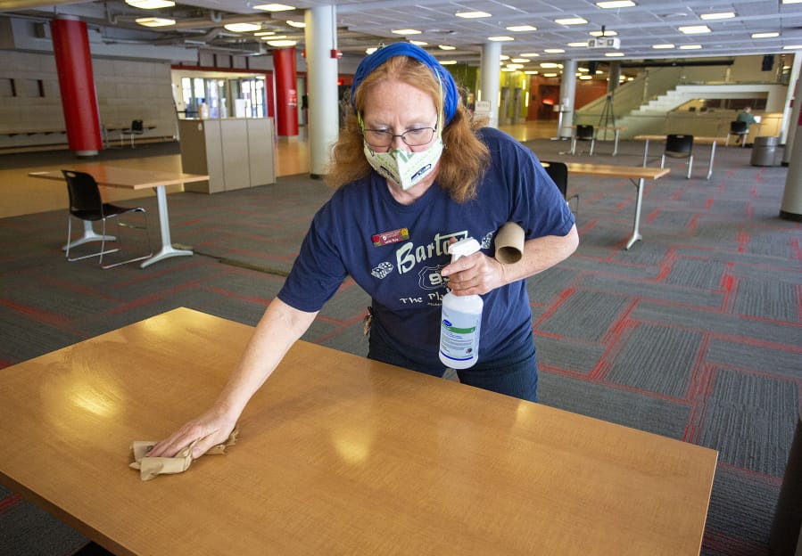 Custodial supervisor Leila Ruiz sanitizes a table in a lounge at the Compton Union Building on Friday, Aug. 28, 2020, at Washington State University in Pullman, Wash. Tables in the building are being sanitized once an hour. The university has launched the Cougs Cancel COVID campaign after a surge in the number of students testing positive for COVID-19 this week.