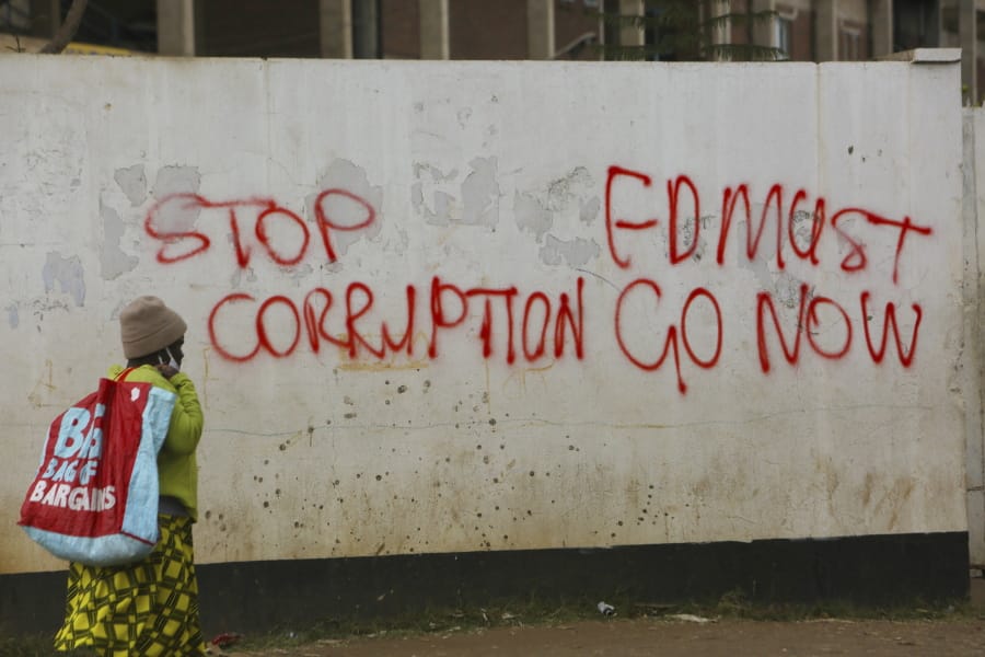 A woman walks past a wall with graffiti calling on the government to stop corruption in this Monday, June, 15, 2020 photo.