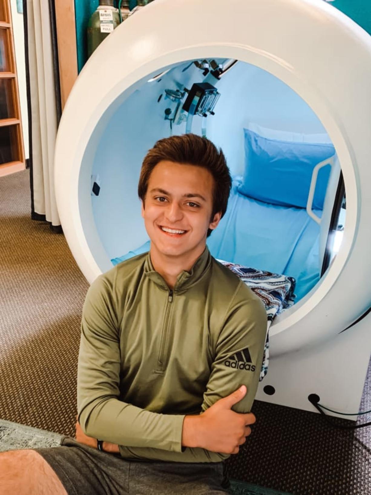 Alec Marshall poses in front of a hard-shell hyperbaric chamber at In Light Hyperbarics. The chamber is called &quot;Moby Dick&quot; because it looks like a big, white whale.