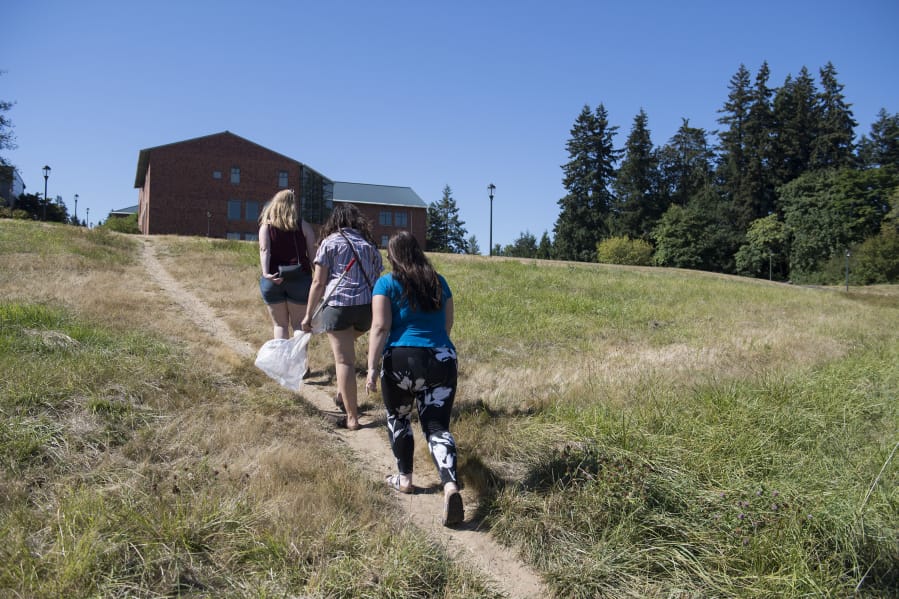Washington State University Vancouver biology graduate students Samantha Bussan, left, Rebekah Gaxiola and Kelsey King take a shortcut after visiting a campus meadow they intend to replant with native wildflowers.
