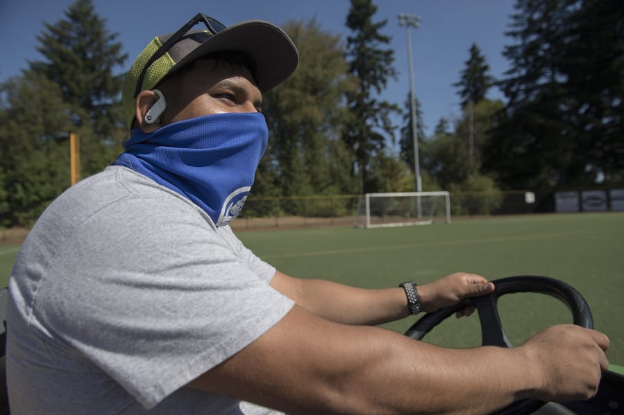 Roy Flores, a grounds maintenance specialist at Luke Jensen Sports Park, steps behind the wheel as he prepares to sweep a soccer field on a recent weekday.