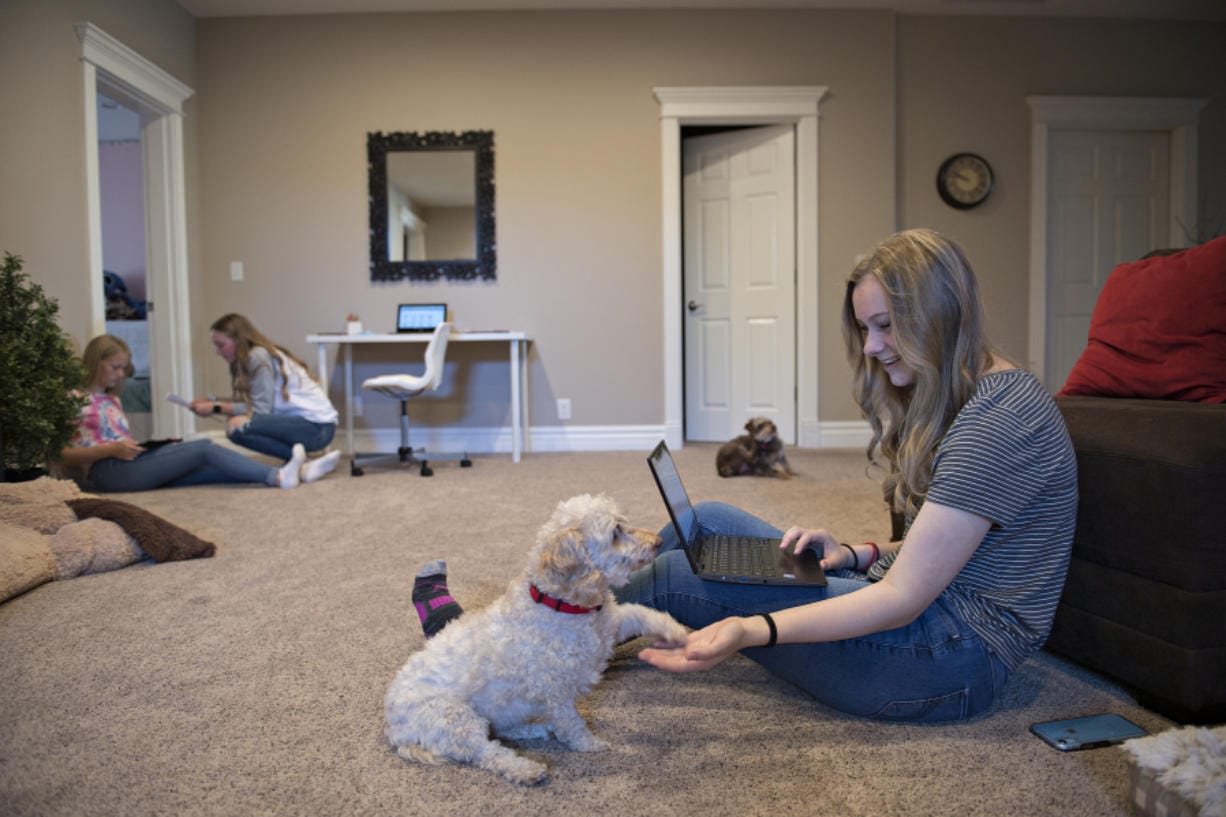 Eighth grader Taryn Albrecht, 13, left, gears up for the first day of school with help from her sister, Nina, 17, who is a senior, while their other sister, Kira, 15, who is a sophomore, shares a moment with their dog, Charlie, 8, at their Vancouver home Tuesday morning. Classes continued to be held online as concerns about COVID-19 shut down schools.