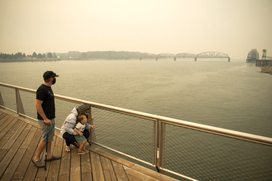 Brent McCarthy, from left, and Marissa Matthews, play on the pier Thursday at The Waterfront Vancouver with their son Xavier, 2. The family lives outside of Salem, Ore., and evacuated Tuesday to escape the smoke and fire risk. Matthews has cancer and is extra sensitive to the smoke, so although their area was still on level 2 evacuation, they decided to leave early to stay safe.