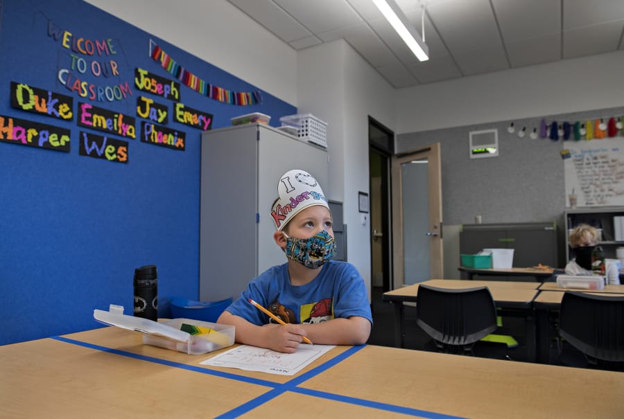 Kindergartner Phoenix Winmil, 5, wears a hat that says &quot;I Love Kindergarten&quot; as he tackles schoolwork on the second day of classes at Sifton Elementary School on Tuesday afternoon. Students are isolated to their own table rather than the typical arrangement of four students to one large desk. Students are also given their own sets of supplies that can be disinfected after class is over.