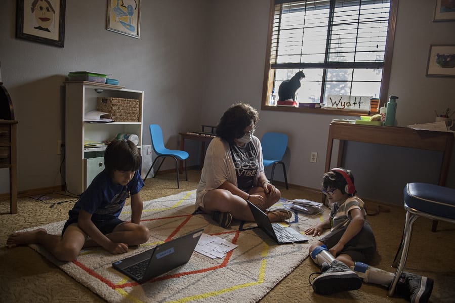 Rowan Lovato, 7, left, tackles schoolwork on his laptop while joined by tutor, Cheryl Davey, his twin brother, Wyatt, 7, and family cat, Jolene, at their Vancouver home Friday afternoon. The Lovato family is struggling to navigate digital learning, with one son with cerebral palsy, single mother Jill Lovato working full time and other obstacles.