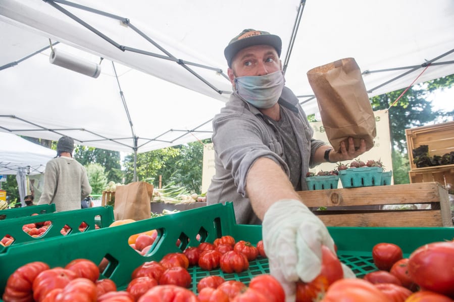 Aaron Stubbs grabs sauce tomatoes for a customer at the Quackenbush Farm booth at the Vancouver Farmers Market on Saturday. Stubbs said the booth actually fared better this summer at the market, likely due to preordered products.