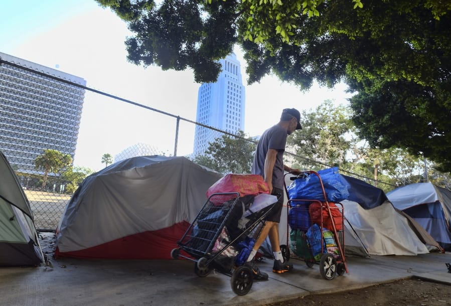FILE - In this Monday, July 1, 2019, file photo, a homeless man moves his belongings from a street behind Los Angeles City Hall as crews prepared to clean the area. Over three days and nights this week, census takers are going to shelters, soup kitchens, mobile food van stops and other places across the U.S. where homeless people often gather. They will follow that with visits to encampments, under bridges, transit stations and other places where people live outside.