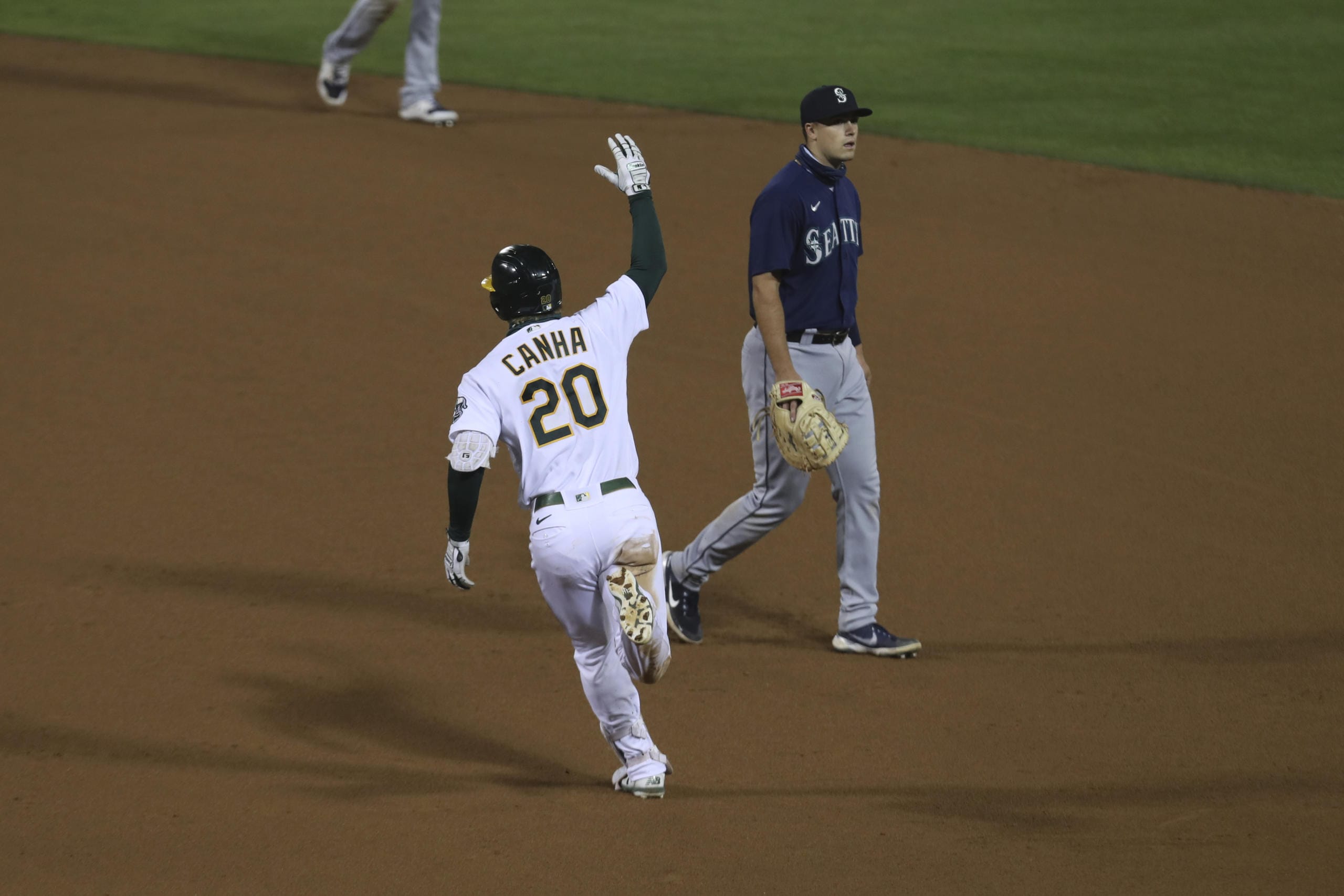 Oakland Athletics' Mark Canha (20) celebrates after hitting a game winning home run, while running past Seattle Mariners' Evan White during the 10th inning of a baseball game in Oakland, Calif., Friday, Sept. 25, 2020.