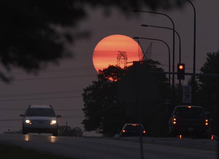 Traffic flows on Townline Road as a hazy sun sets in Vernon Hills, Ill,, Tuesday, Sept. 15, 2020.   The smoke from dozens of wildfires in the western United States has now blanket much of the county along with parts of Mexico and Canada, as residents thousands of miles away on the East Coast are being treated to unusually hazy skies and remarkable sunsets.