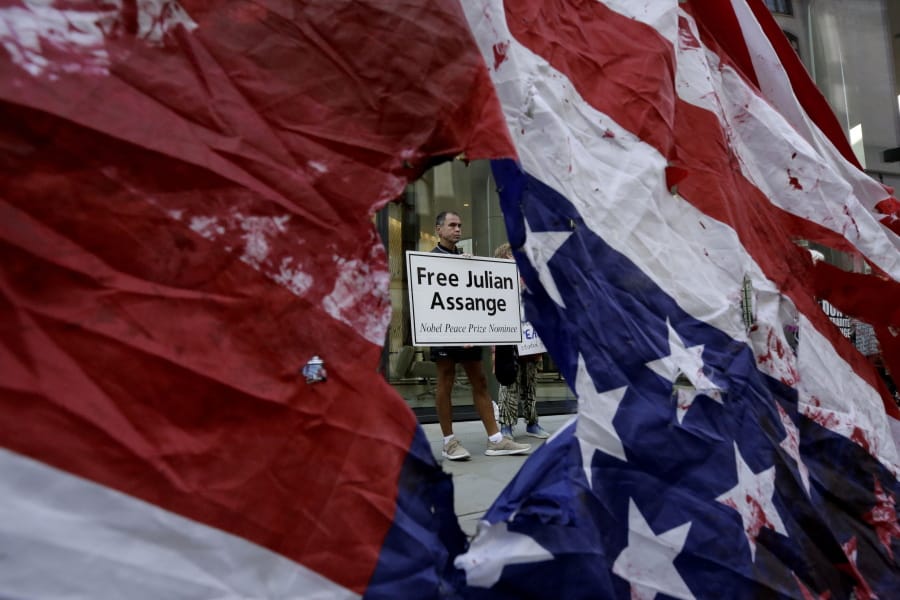 A supporter of WikiLeaks founder Julian Assange is seen through a hole torn in a defaced U.S. flag during a protest outside the Central Criminal Court, the Old Bailey, in London, Monday, Sept. 14, 2020. The London court hearing on Assange&#039;s extradition from Britain to the United States resumed Monday after a COVID-19 test on one of the participating lawyers came back negative, WikiLeaks said Friday.