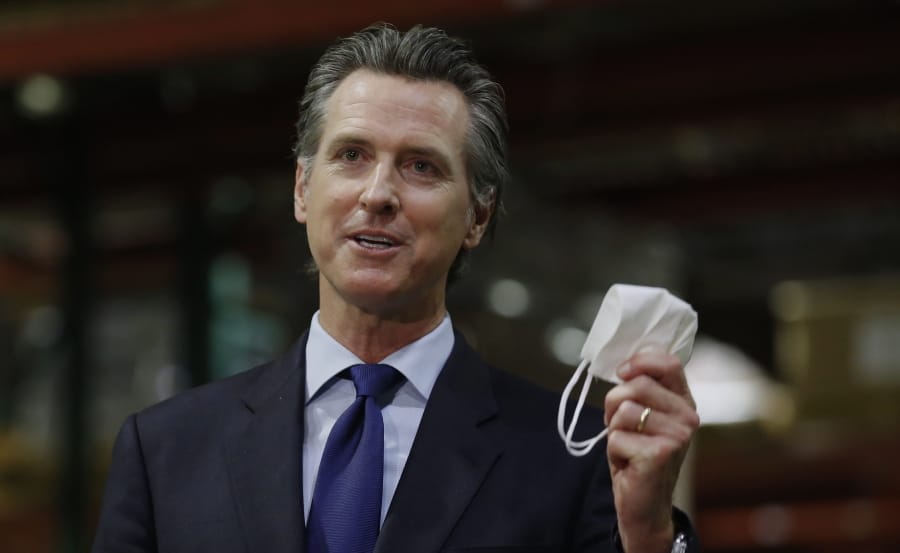 FILE - In this June 26, 2020 file photo, Gov. Gavin Newsom holds a face mask as he urges people to wear them to fight the spread of the coronavirus during a news conference in Rancho Cordova, Calif. On Saturday, Sept. 26, 2020, Newsom signed a law that requires the state to house transgender prisoners based on their gender identity.