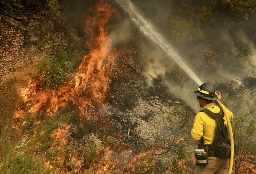 A firefighter puts out a hot spot along Highway 38 northwest of Forrest Falls, Calif., as the El Dorado Fire continues to burn Thursday afternoon, Sept. 10, 2020. The fire started by a device at a gender reveal party on Saturday.