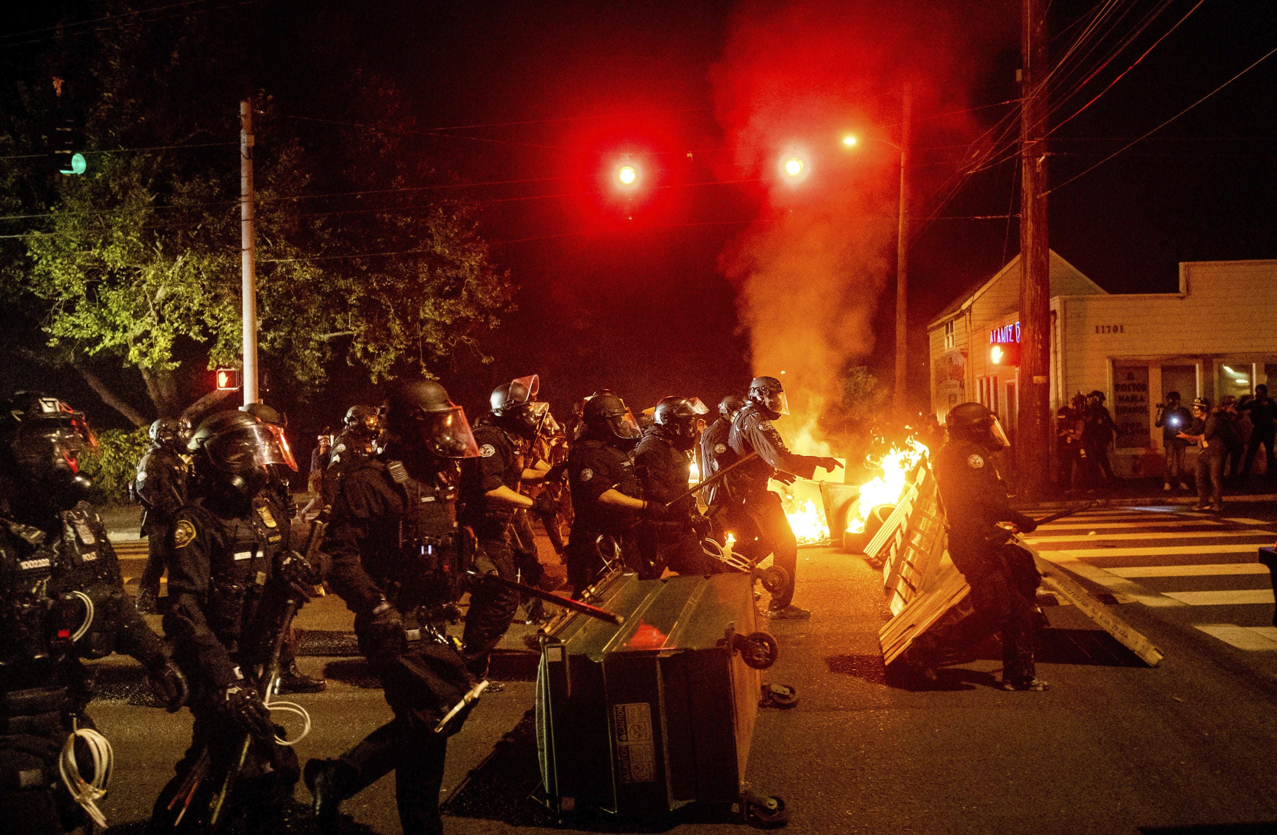 Police officers pass a fire lit by protesters on Saturday, Sept. 5, 2020, in Portland, Ore. Hundreds of people gathered for rallies and marches against police violence and racial injustice Saturday night in Portland, Oregon, as often violent nightly demonstrations that have happened for 100 days since George Floyd was killed showed no signs of ceasing.