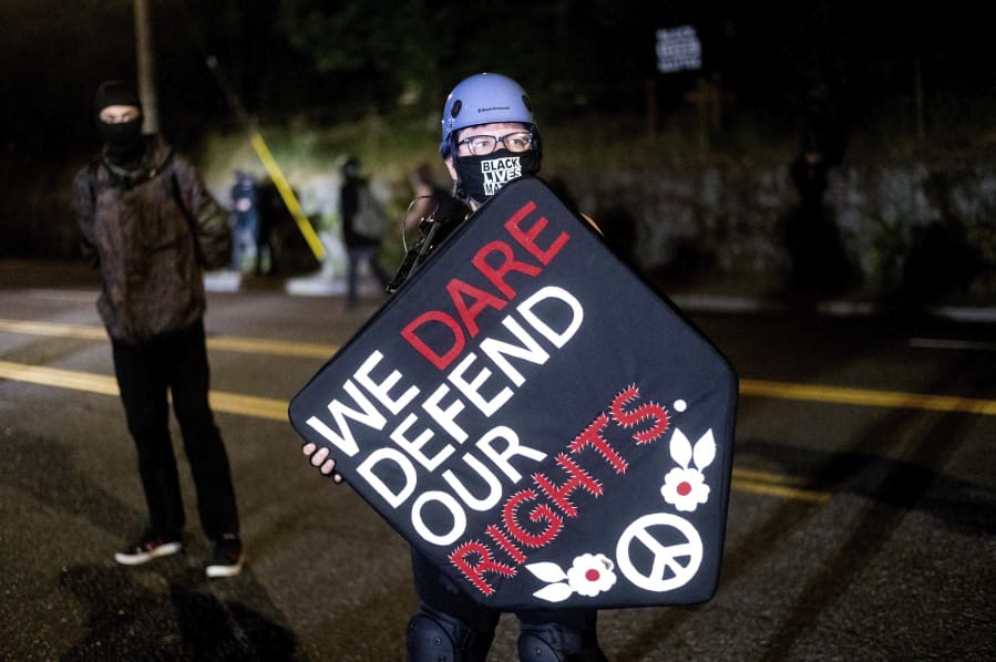 Stacy Kendra Williams holds a shield while facing off against police at the Penumbra Kelly Building on Thursday, Sept. 3, 2020, in Portland, Ore. This weekend Portland will mark 100 consecutive days of protests over the May 25 police killing of George Floyd.