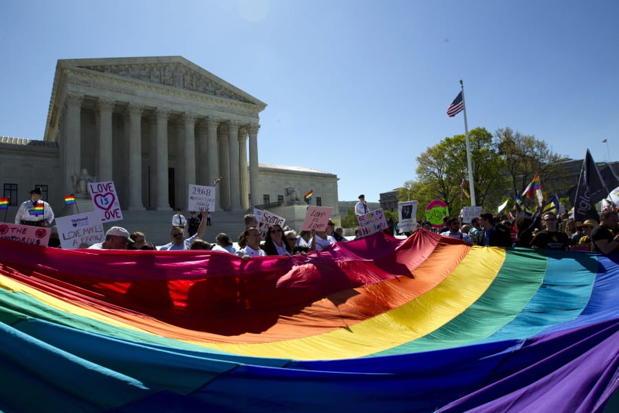 FILE - In this April 28, 2015 file photo, demonstrators stand in front of a rainbow flag of the Supreme Court in Washington. In 2019, there were slightly less than 1 million same-sex couple households in the U.S., and a majority of those couples were married. New figures released Thursday, Sept. 17, 2020 by the U.S. Census Bureau shows that of the 980,000 same-sex couple households, 58% were married couples and 42% were unmarried partners.