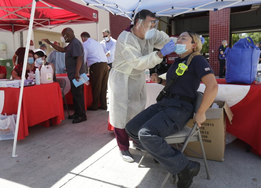 FILE - In this Aug. 6, 2020, file photo, Hialeah Fire Department Firefighter-Paramedic Laura Nemoga, right, winces as medical assistant Jesus Vera performs a COVID-19 test at Hialeah Fire Station #1, in Hialeah, Fla. The torrid coronavirus summer across the Sun Belt is easing after two disastrous months that brought more than 35,000 deaths.