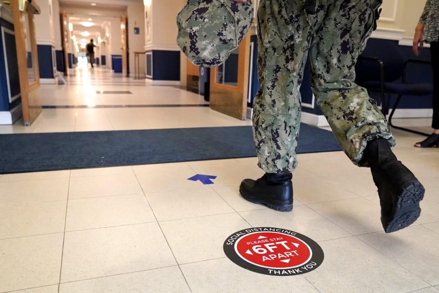A social distancing sign is seen on the floor as a midshipman walks to class at Luce Hall at the U.S. Naval Academy, Monday, Aug. 24, 2020, in Annapolis, Md. Under the siege of the coronavirus pandemic, classes have begun at the Naval Academy, the Air Force Academy and the U.S. Military Academy at West Point. But unlike at many colleges around the country, most students are on campus and many will attend classes in person.