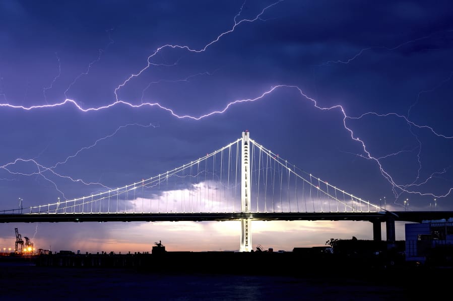FILE - In this Aug. 16, 2020, file photo, lightning forks over the San Francisco-Oakland Bay Bridge as a storm passes over Oakland, Calif. Numerous lightning strikes sparked brush fires throughout the region.