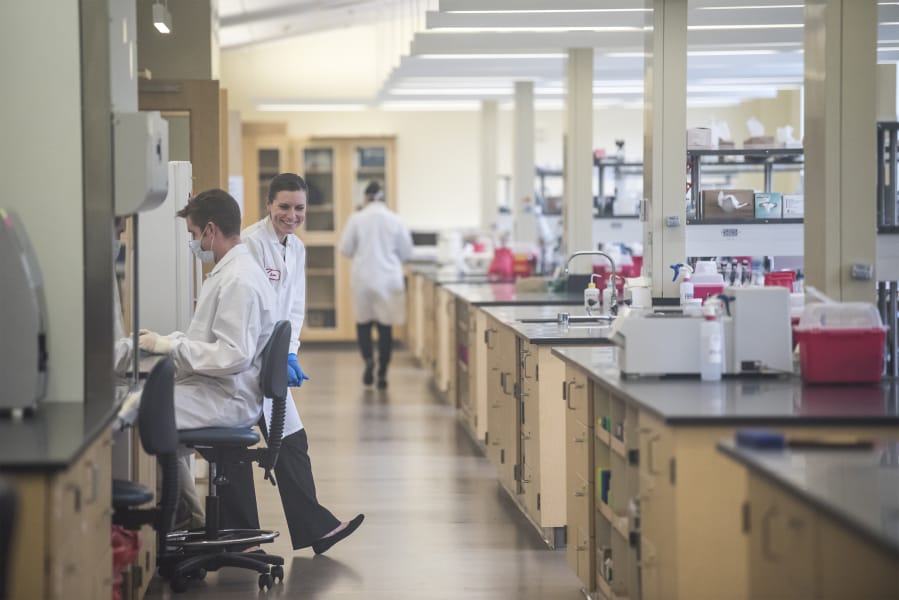 Forensic scientists Justin Knoy, left, and Laura Kelly laugh while working on a DNA sample at the Washington State Patrol Vancouver Crime Lab in March 2019. A new segment of the lab, aimed at clearing the statewide backlog of sexual assault kits, opened in June but is not fully operational due to ongoing COVID-19 testing demands.