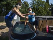 Laura Thornquist, left, demonstrates how she has been coaching teammates while the coronavirus pandemic has kept them off the lake. She corrects teammate Britten Witherspoon&#039;s form as she paddles in a water trough in Thornquist&#039;s Woodland backyard.