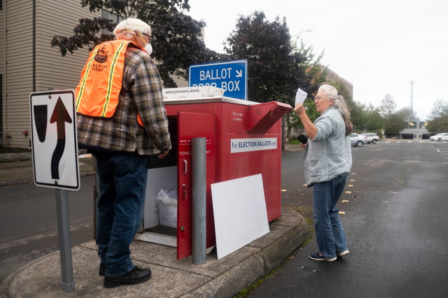 Vancouver resident Sharon Grammar, right, drops off her ballot while elections worker John Waterbury collects ballots from an official ballot drop box near the Clark County Elections Office in downtown Vancouver on Saturday morning.