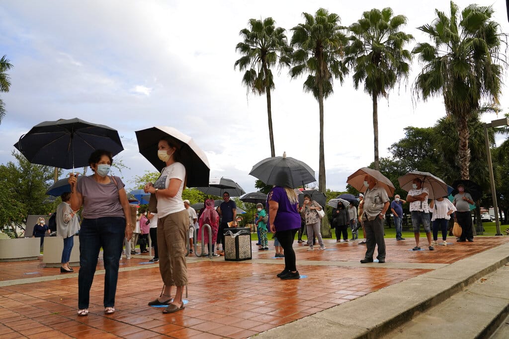 People wait in line in the rain outside of an early voting site, Monday, Oct. 19, 2020, in Miami. Florida begins in-person early voting in much of the state Monday. With its 29 electoral votes, Florida is crucial to both candidates in order to win the White House.