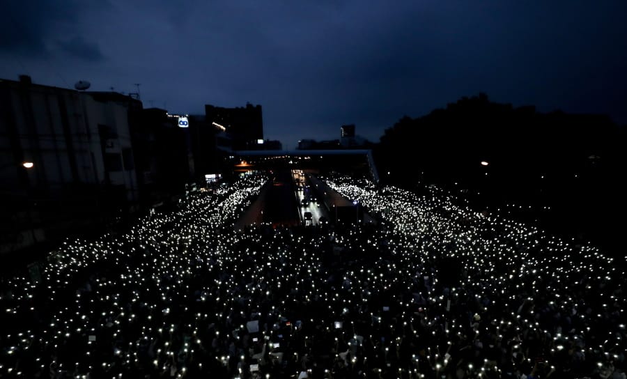 Pro-democracy activists wave mobile phones with lights during a demonstration at Kaset intersection, suburbs of Bangkok, Thailand, Monday, Oct. 19, 2020. Thai authorities worked Monday to stem a growing tide of protests calling for the prime minister to resign by threatening to censor news coverage, raiding a publishing house and attempting to block the Telegram messaging app used by demonstrators.
