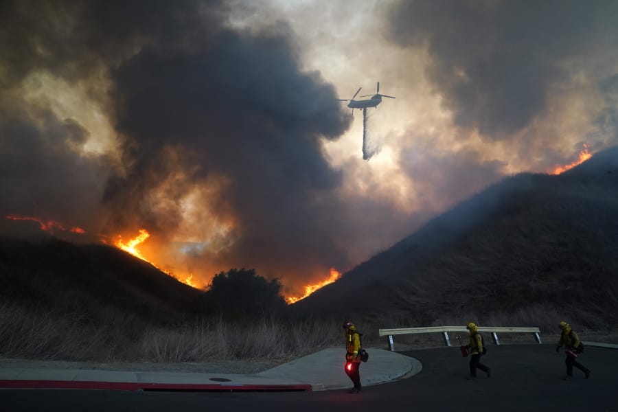 A helicopter drops water as firefighters walk with drip torches to set a backfire against the Blue Ridge Fire on Tuesday, Oct. 27, 2020, in Chino Hills, Calif. Facing extreme wildfire conditions this week that included hurricane-level winds, the main utility in Northern California cut power to nearly 1 million people while its counterpart in Southern California pulled the plug on just 30 customers to prevent power lines and other electrical equipment from sparking a blaze. (AP Photo/Jae C.