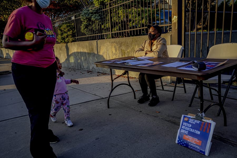 A woman and child walk past Laurae Caruth, right, volunteer with Christian Cultural Center Social Justice Initiative&#039;s voter registration drive, as she sits at a table where she registers voters, Friday, Sept. 18, 2020, in the Brooklyn borough of New York. &quot;I&#039;m out here volunteering because of how important it is to exercise the right to vote,&quot; Caruth said. In recent election cycles, predominantly Black congregations across the country have launched get-out-the-vote campaigns commonly referred to as &quot;souls to the polls.&quot; But instead of packing buses and vans to shuttle people to early voting sites this year, church leaders say they are organizing caravans for absentee ballot drop-offs and in-person early voting.