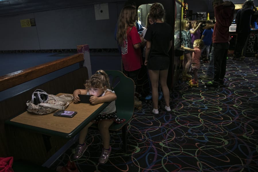 A girl is immersed in a smartphone game while others play in an arcade at a skating rink, Saturday, Aug. 1, 2020, in Anna, Ill.