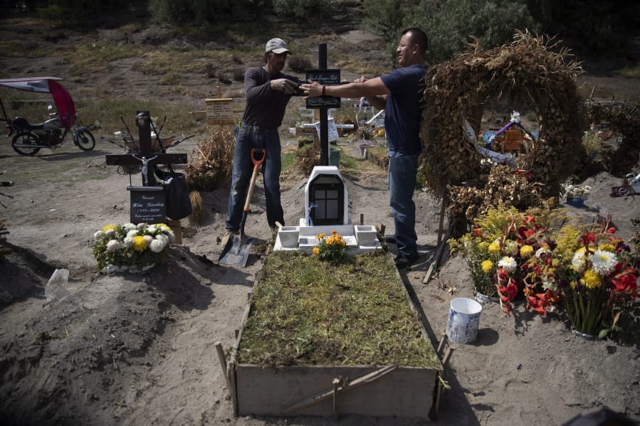 Cemetery worker Jorge Arvizu, left, helps a family member place a plaque on the grave of Vicente Dominguez who died of complications related to the new coronavirus, at the municipal cemetery Valle de Chalco, on the outskirts of Mexico City, Tuesday, Oct. 20, 2020. Mexican families traditionally flock to local cemeteries to honor their dead relatives as part of the &quot;Dia de los Muertos,&quot; or Day of the Dead celebrations, but according to authorities the cemeteries will be closed this year to help curb the spread of COVID-19.