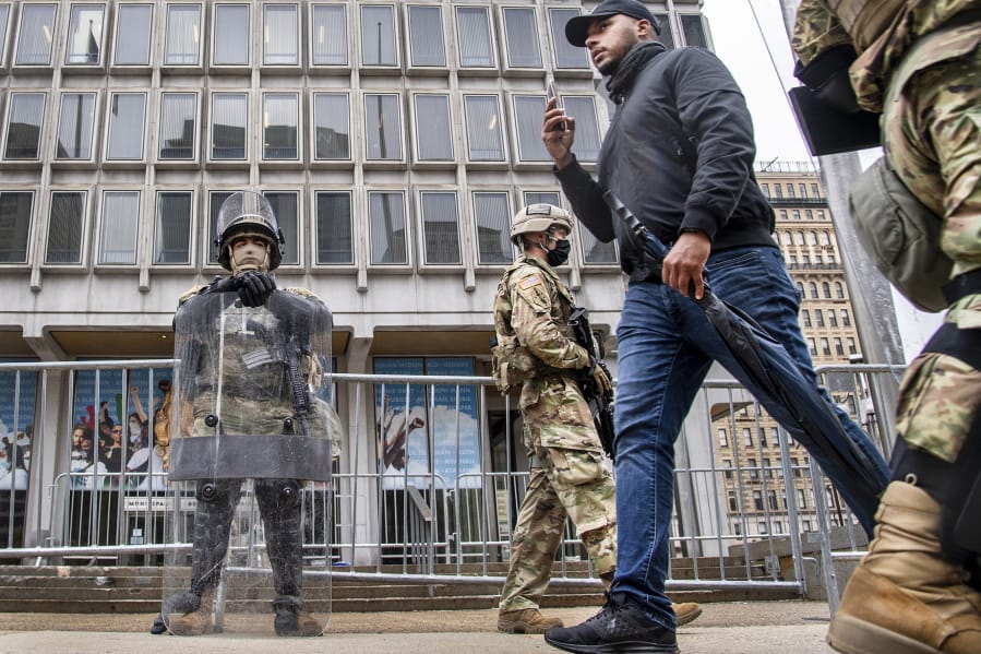 An unidentified pedestrian walks between members of the National Guard as they stand guard in front of the Philadelphia Municipal Services Building in Philadelphia, Pa., Friday, Oct. 30, 2020. (Jose F.
