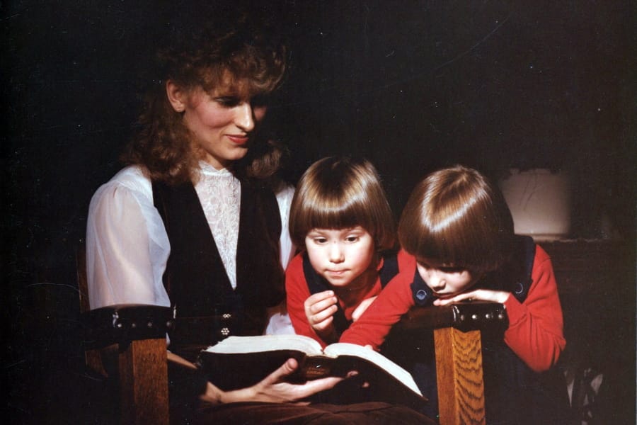 This image provided by Coral Theill, shows Theill with her twin girls in 1984, reading from their family Bible.