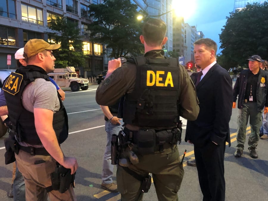 In this Wednesday, June 3, 2020, photo Acting Drug Enforcement Administrator Timothy Shea, right, visits with DEA agents at a checkpoint in Washington. More than 1,500 people have been arrested in the last three months as part of a Drug Enforcement Administration project focusing on violent crime. The initiative, nicknamed Project Safeguard, comes as President Donald Trump has touted similar operations as a much-needed answer to a spike in crime. It&#039;s also to showcase what he says is his law-and-order prowess, claiming he&#039;s countering rising crime in cities run by Democrats. Acting DEA Administrator Tim Shea tells the AP that since the operation launched in August, 1,521 people have been arrested in both state and federal cases in cities across the U.S. and 2,135 firearms have been seized.