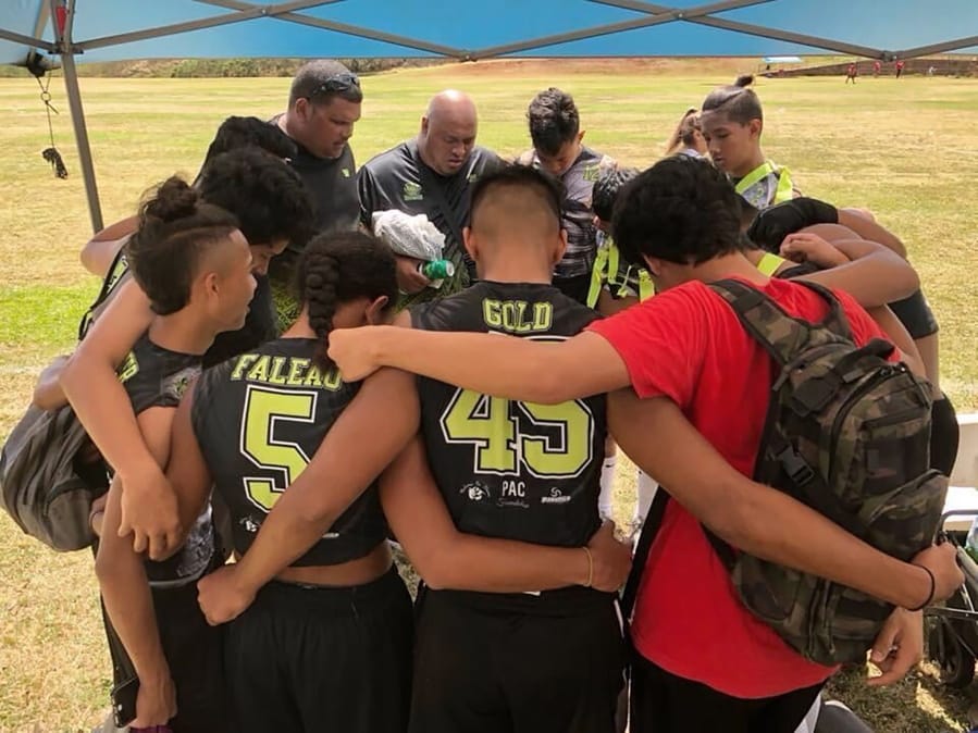 This 2017 photo provided by Ke&#039;ala Aki shows Willie Talamoa, rear center with shaved head, next to Kanohi Aki, rear left, as they pray with players from their 15-and-under flag football team in Honolulu. A Honolulu community is mourning the loss of Talamoa, a mentor, football coach and father figure who died after contracting COVID-19.