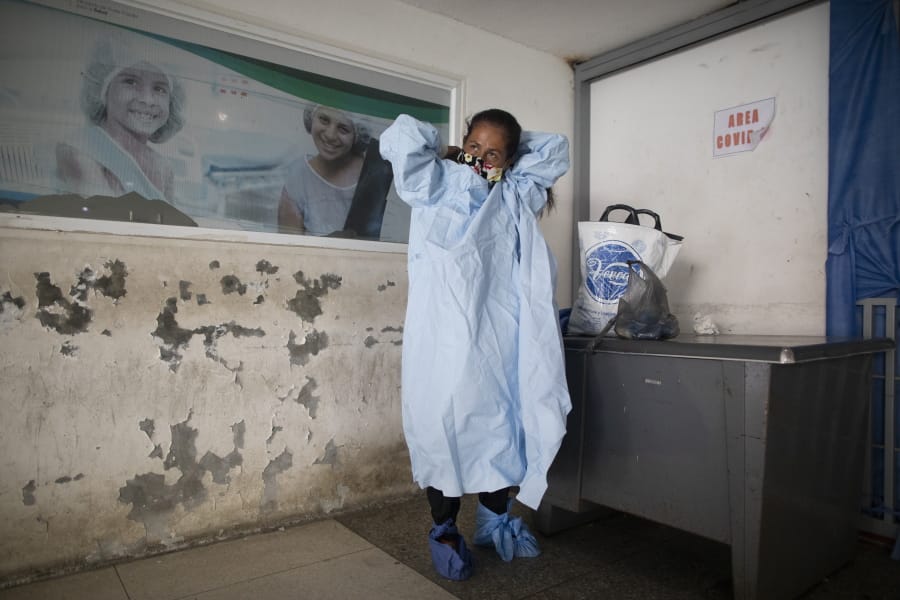 Elena Suazo, a kindergarten cafeteria worker, puts on the protective gear she brought from home, outside the entrance to the COVID-19 wing of Jose Gregorio Hernandez Hospital which used to be the emergency room, as she prepares to enter and care for her 76-year-old hospitalized father, in the Catia neighborhood of Caracas, Venezuela, Thursday, Sept. 24, 2020. In this ruined country, the only way to ensure that he received the care he needed was to do it herself, regardless of the dangers to her own health.