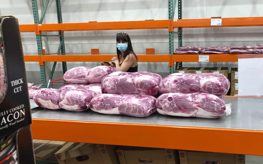 A shopper in a face mask looks over cuts of beef piled up in a cold room for purchase at a Costco warehouse store Tuesday, May 5, 2020, in west Denver.  The U.S. economy rebounded at an even-stronger pace in the July-September quarter than first reported but a resurgence in the coronavirus is expected to slow growth sharply in the current quarter with some analysts even raising the specter of a double-dip recession.